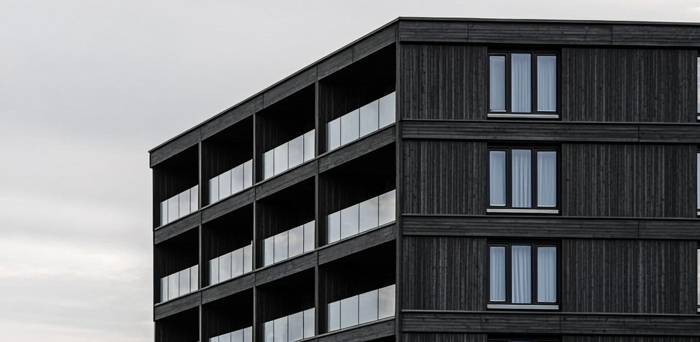 Mørk trebekledd bygning med skarp geometri under grå himmel